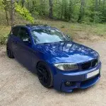 1M išvaizdos Priekinis Bamperis skirtas BMW E81 / E82 / E87 / E88, be PDC, be apiplovimų angų